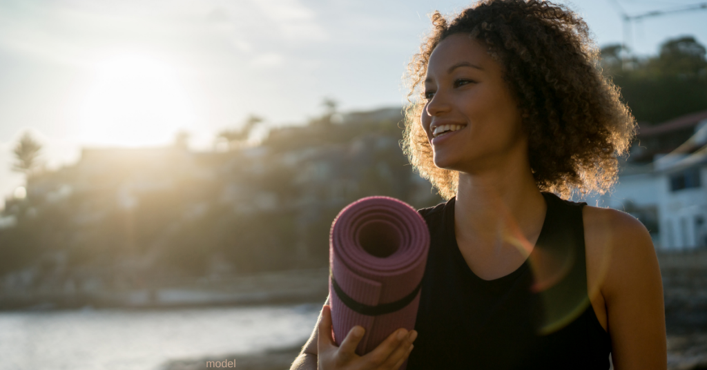 woman with yoga mat in front of beach