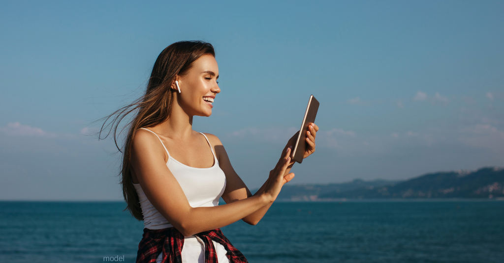 Woman sitting at beach researching BOTOX costs (model)