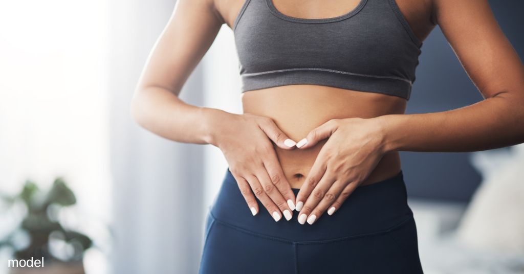 A woman wearing a fitness outfit, touching her stomach (model)