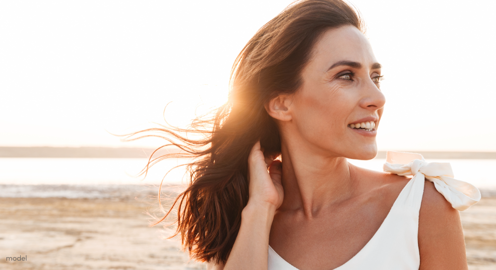 Beautiful woman with long brown hair, hands holding hair back, at the beach.